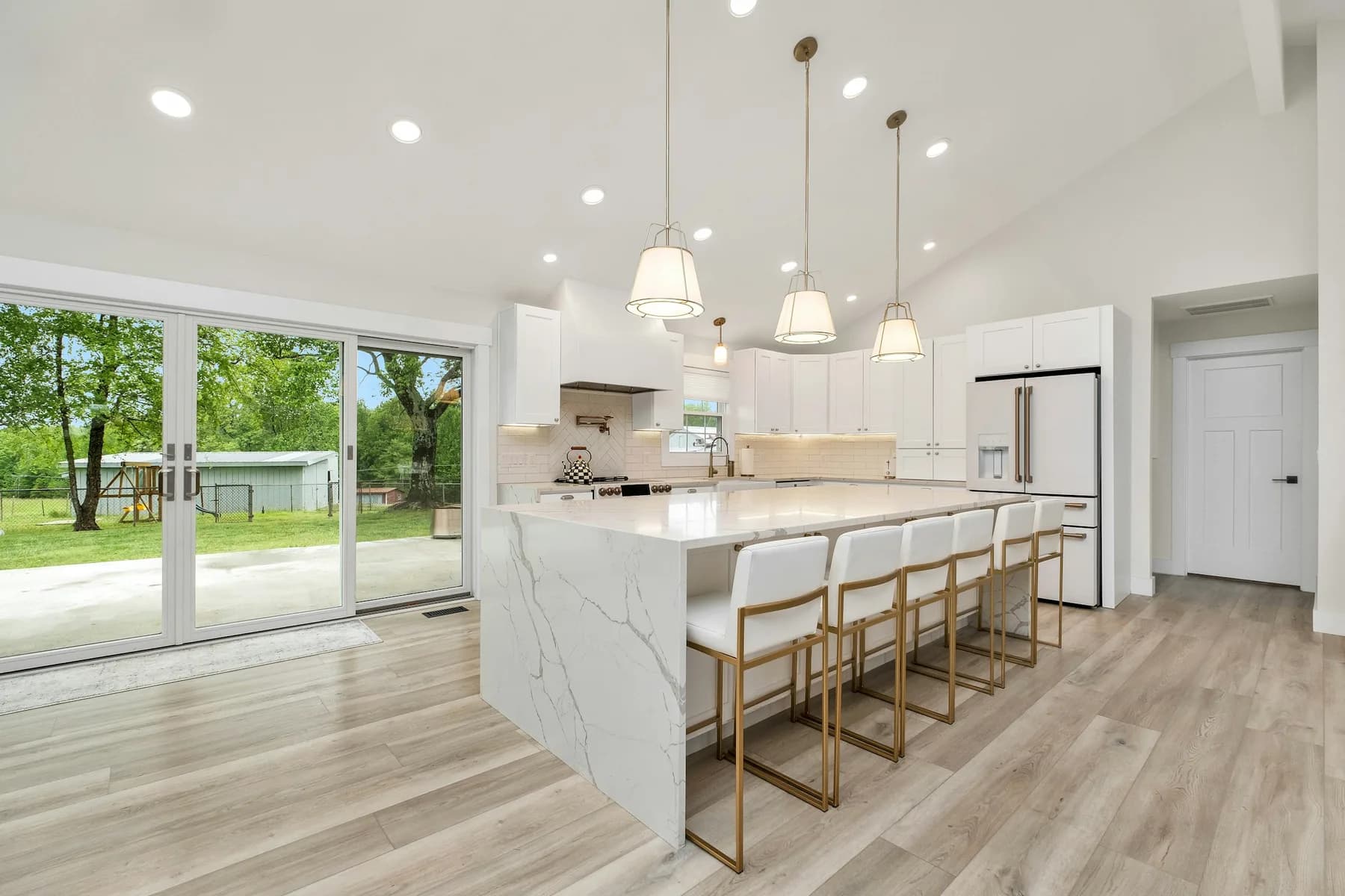 Wide view of open kitchen with marble waterfall island and patio doors beyond