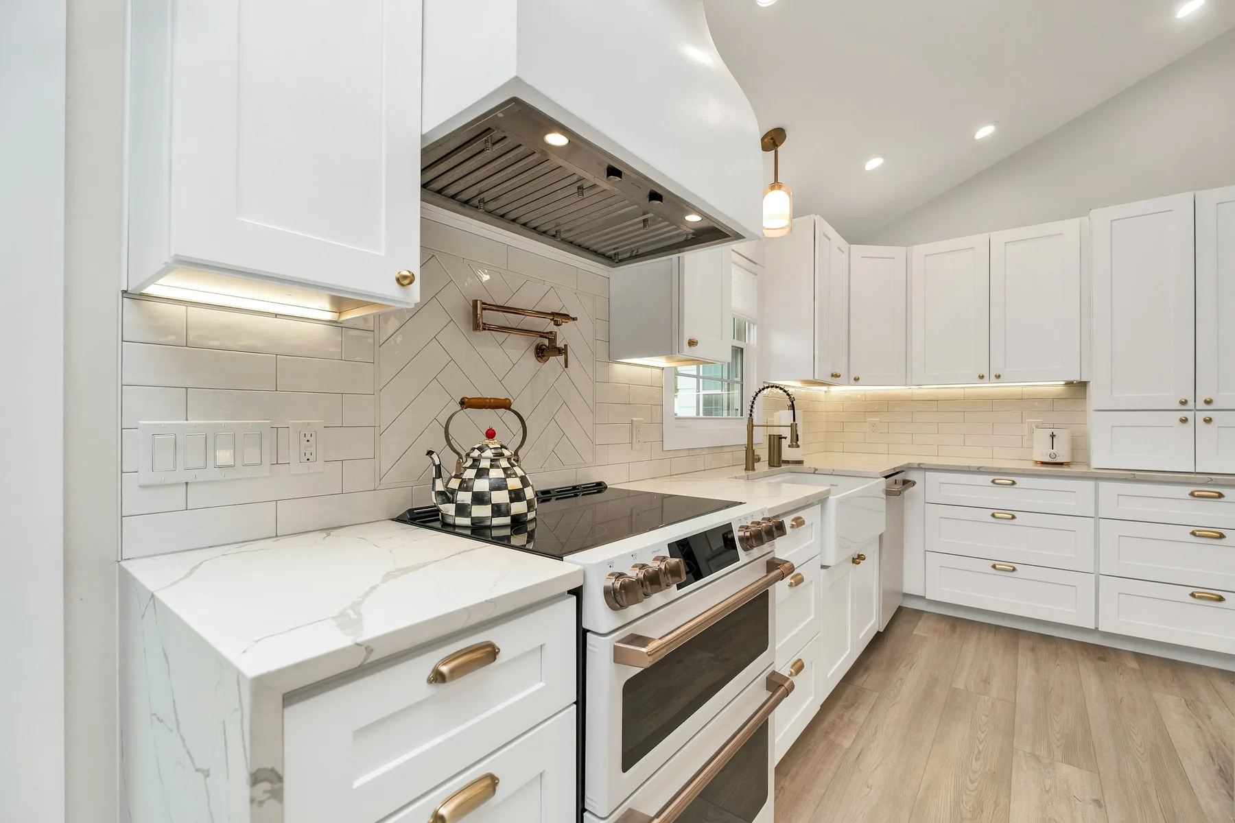 Range with herringbone tile backsplash, brass pot filler and white cabinetry