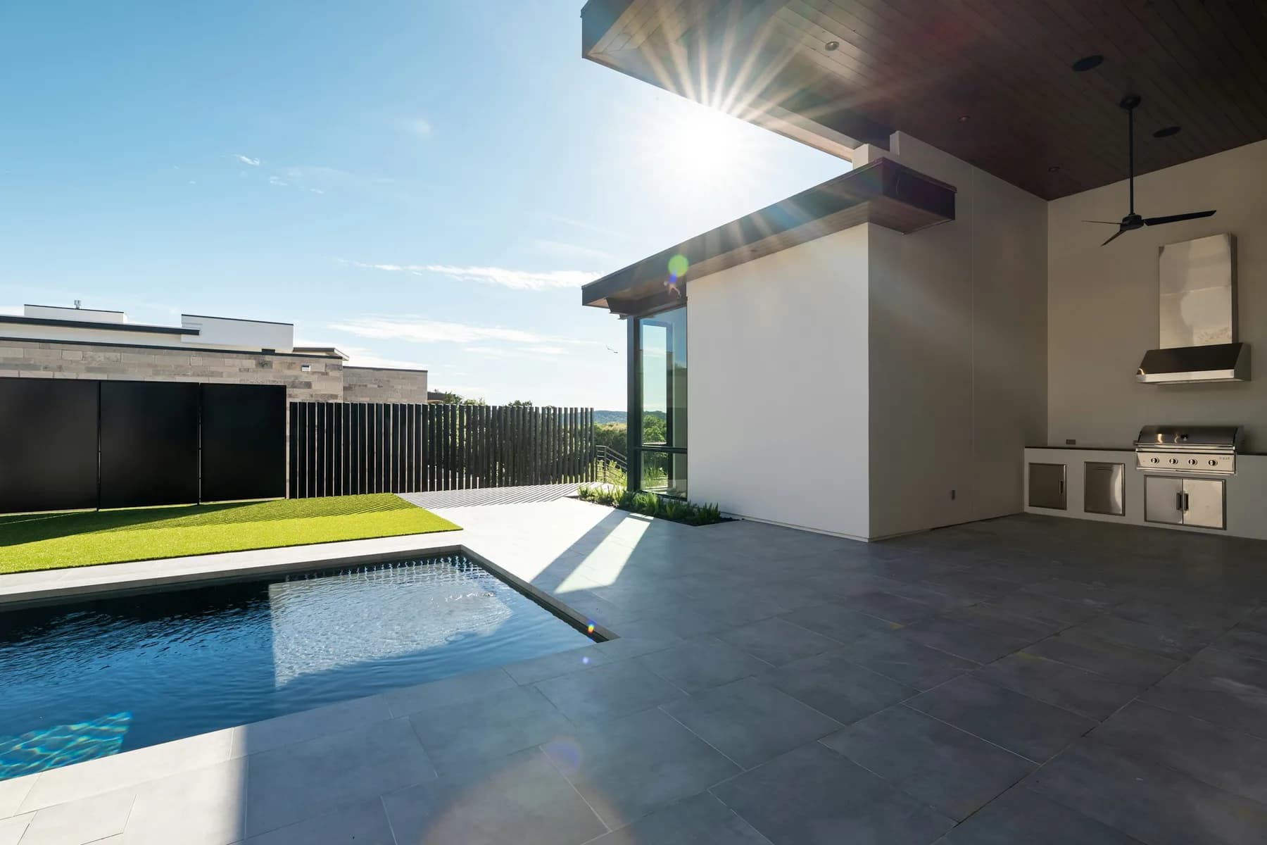 Covered outdoor kitchen with built-in grill overlooking a swimming pool