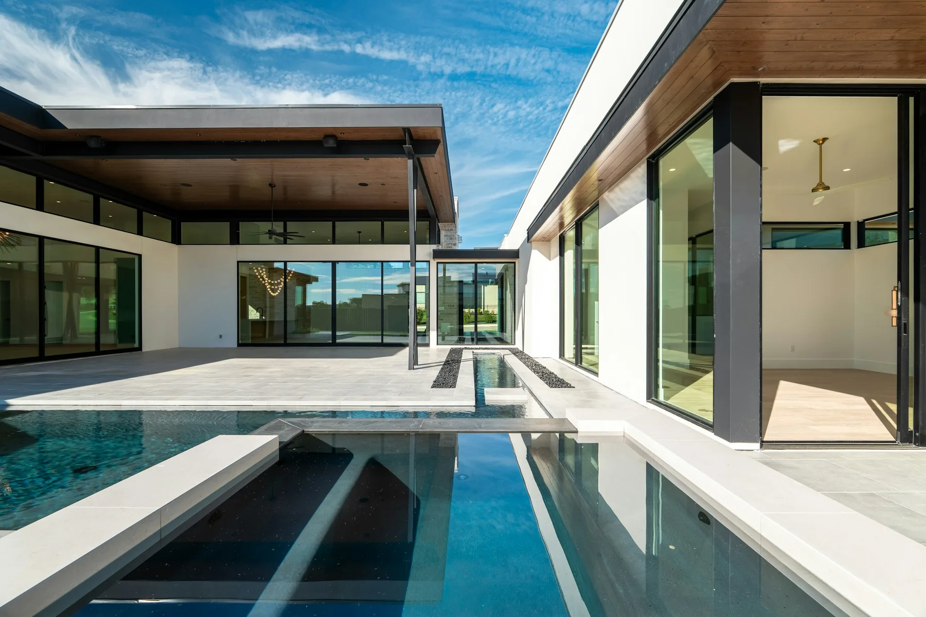 Long swimming pool running between two glazed wings of a modern house