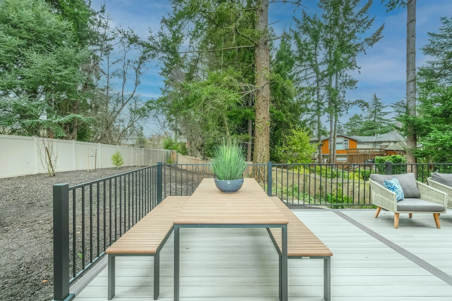 Composite deck terrace with table, planter and black picket railing looking into forest
